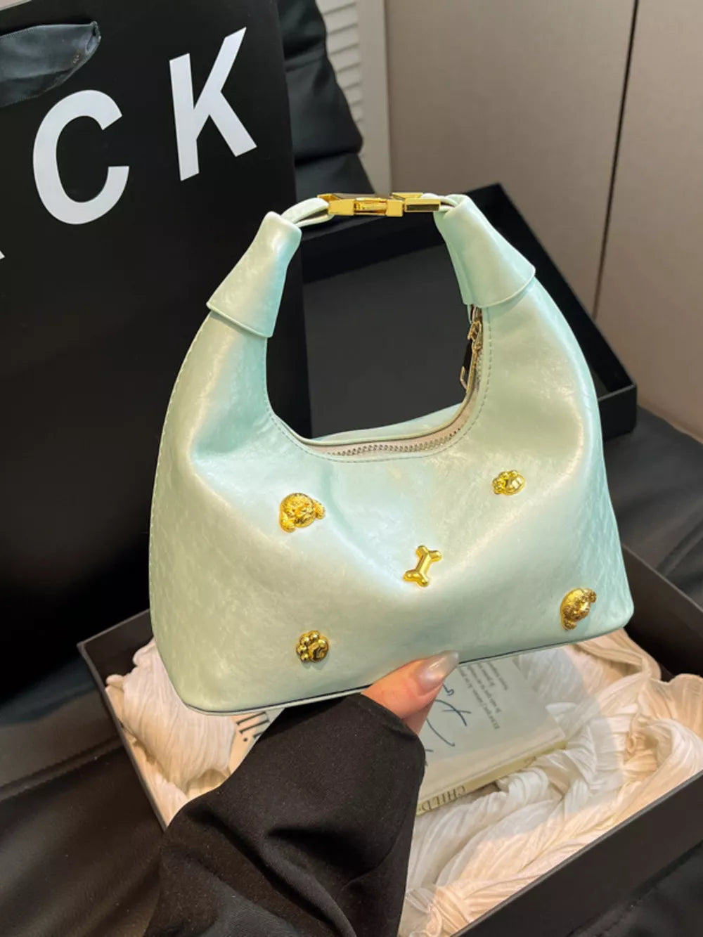Light green hobo bag with gold dog and bone charms and gold hardware.