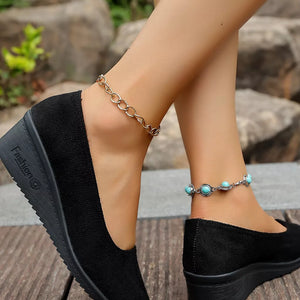 Black wedge slip-on shoes with textured detail and chain anklets with turquoise stones.