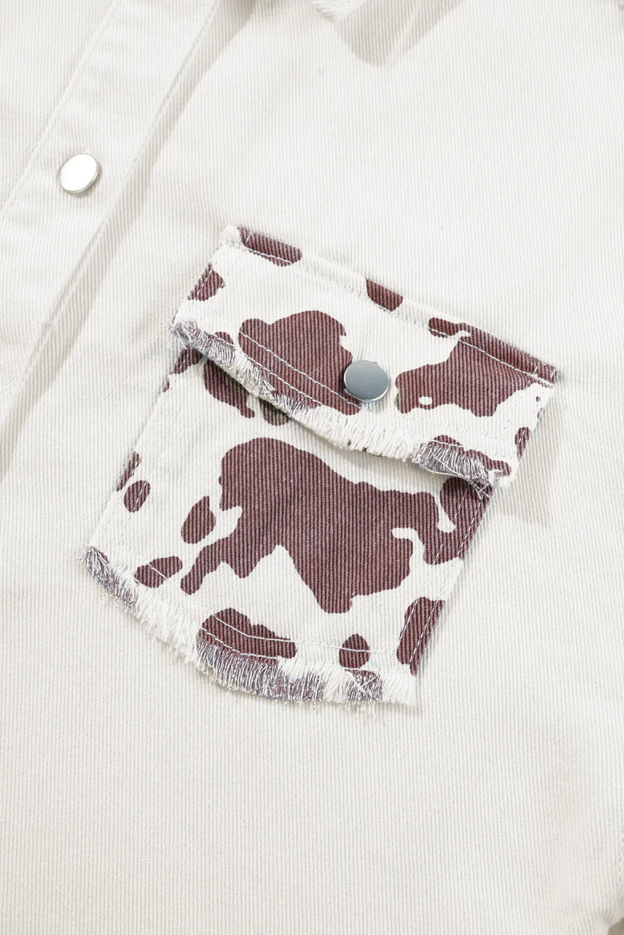 White cow print denim shacket with frayed pocket edges and silver snaps.