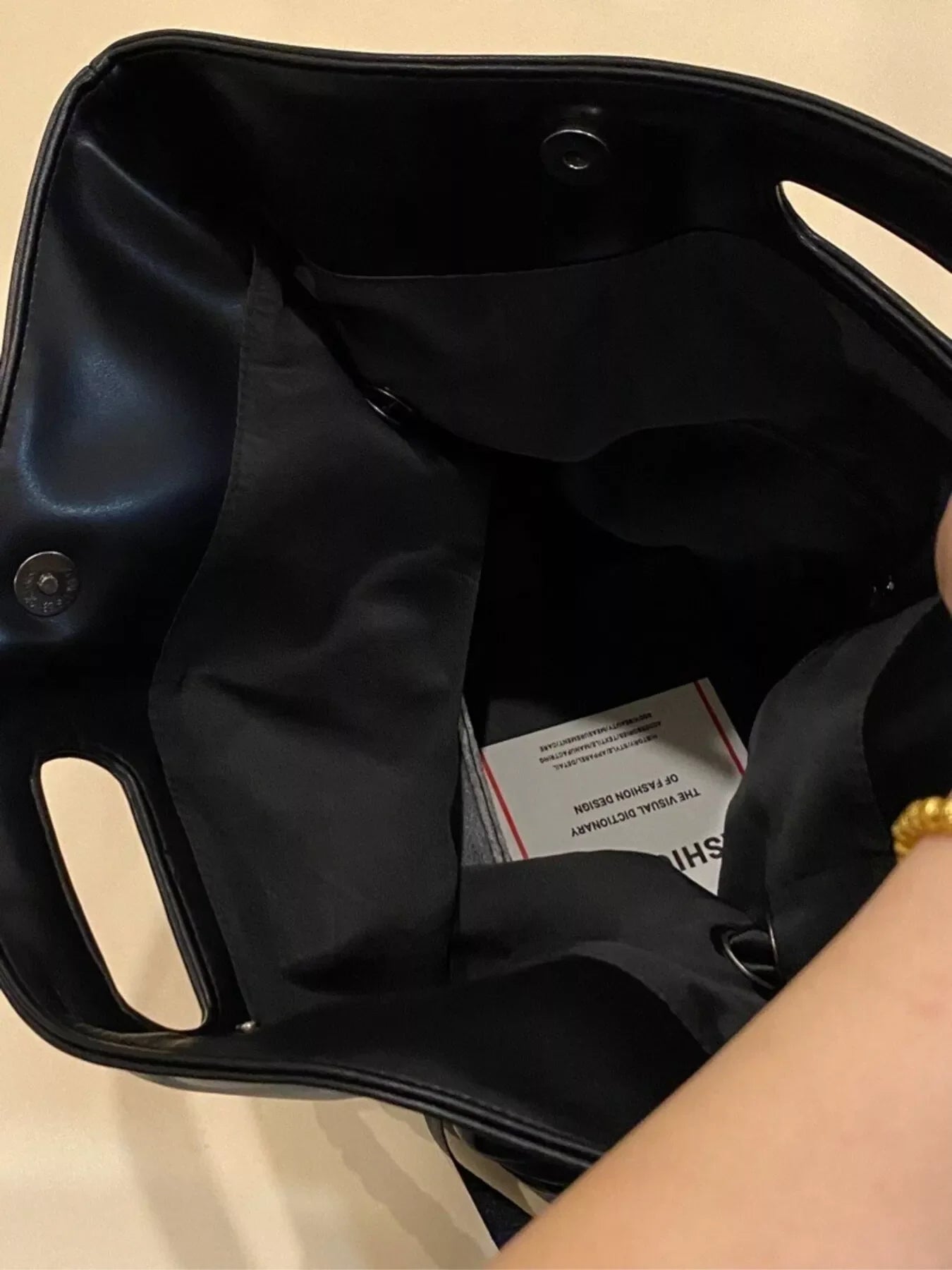 Black oversized PU leather tote bag interior with snap closure and a fashion dictionary tag.