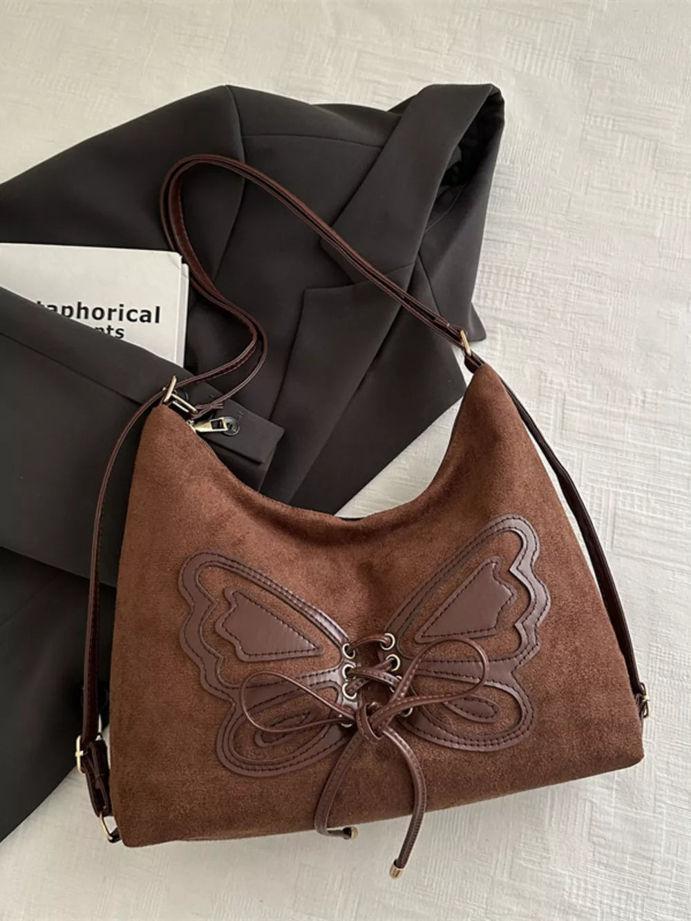 Brown suede half-moon bag with butterfly embellishment and lace-up detail
