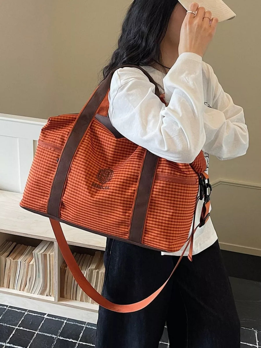 Large orange plaid Oxford travel bag with brown trim and adjustable strap.