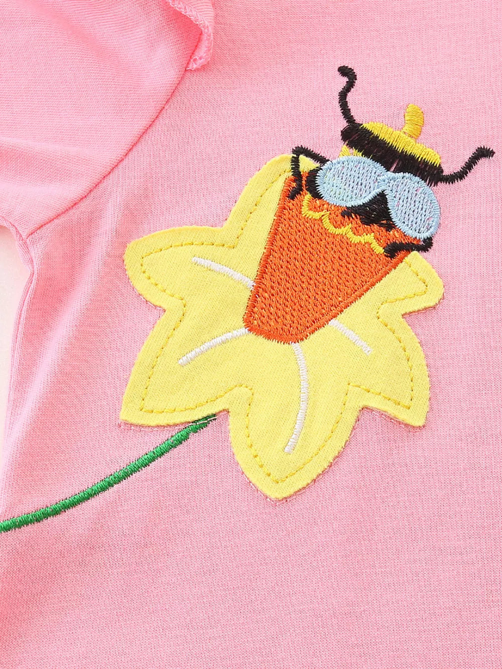 Toddler pink dress with a whimsical bee appliqué wearing sunglasses on a yellow flower.