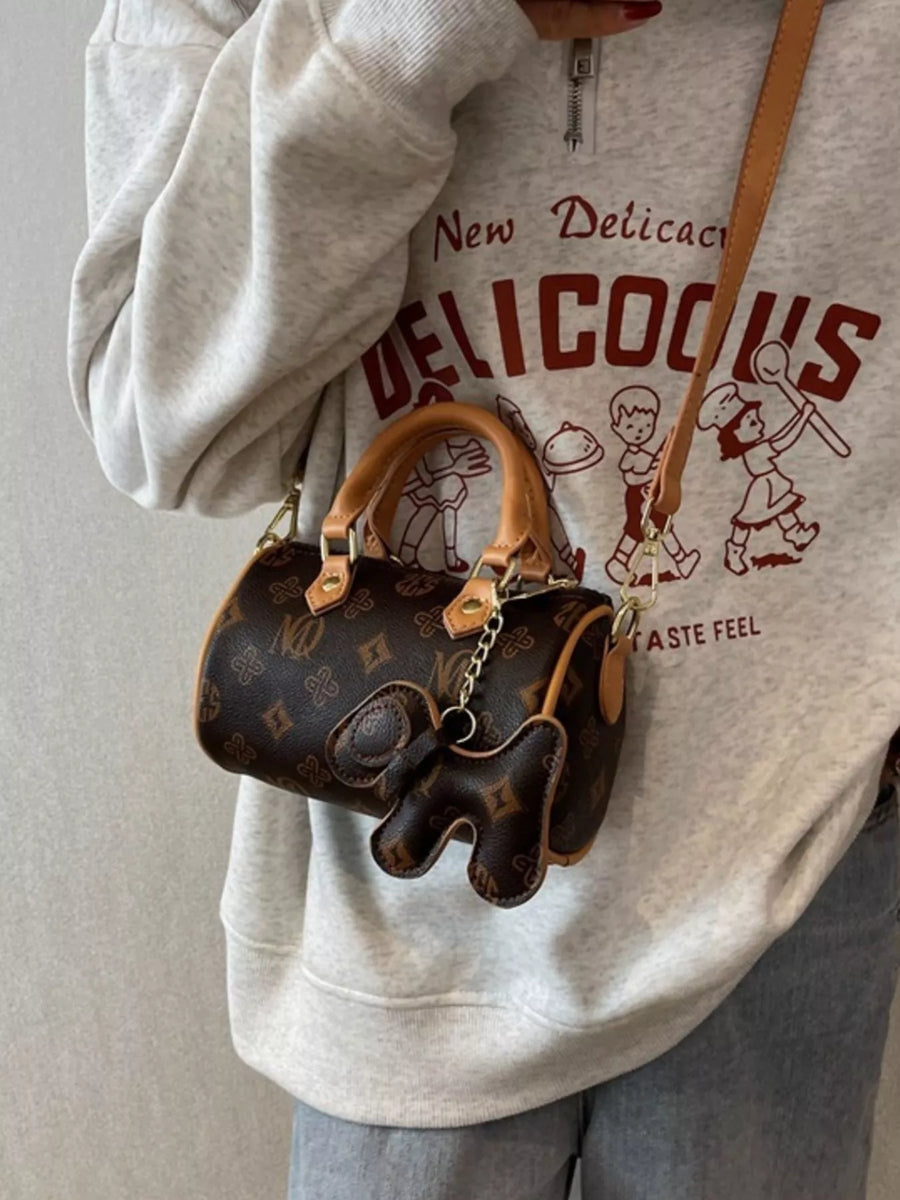 Mini barrel crossbody bag in brown monogram print with elephant charm and tan leather trim.
