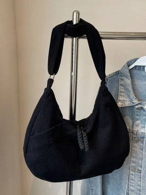 Black corduroy crescent shoulder bag with braided tassel detail and front pocket.