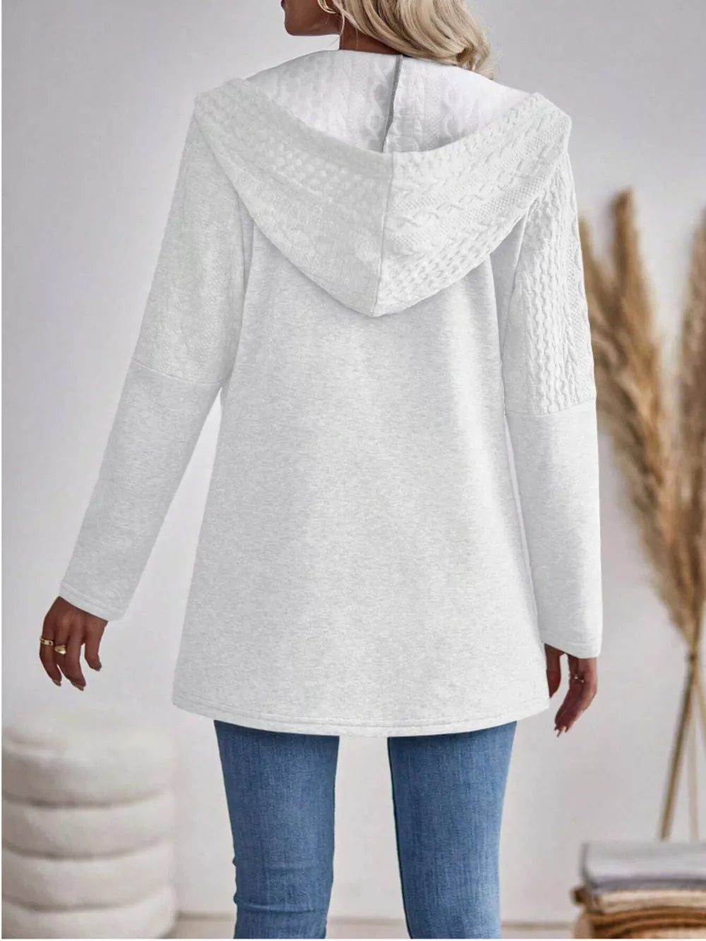 Ivory cable-knit hooded zip jacket with textured details on hood and sleeves.