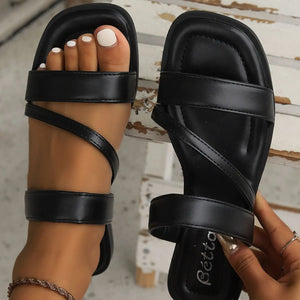 Black leather crossover slides with a minimalist design and wrap-around ankle straps.