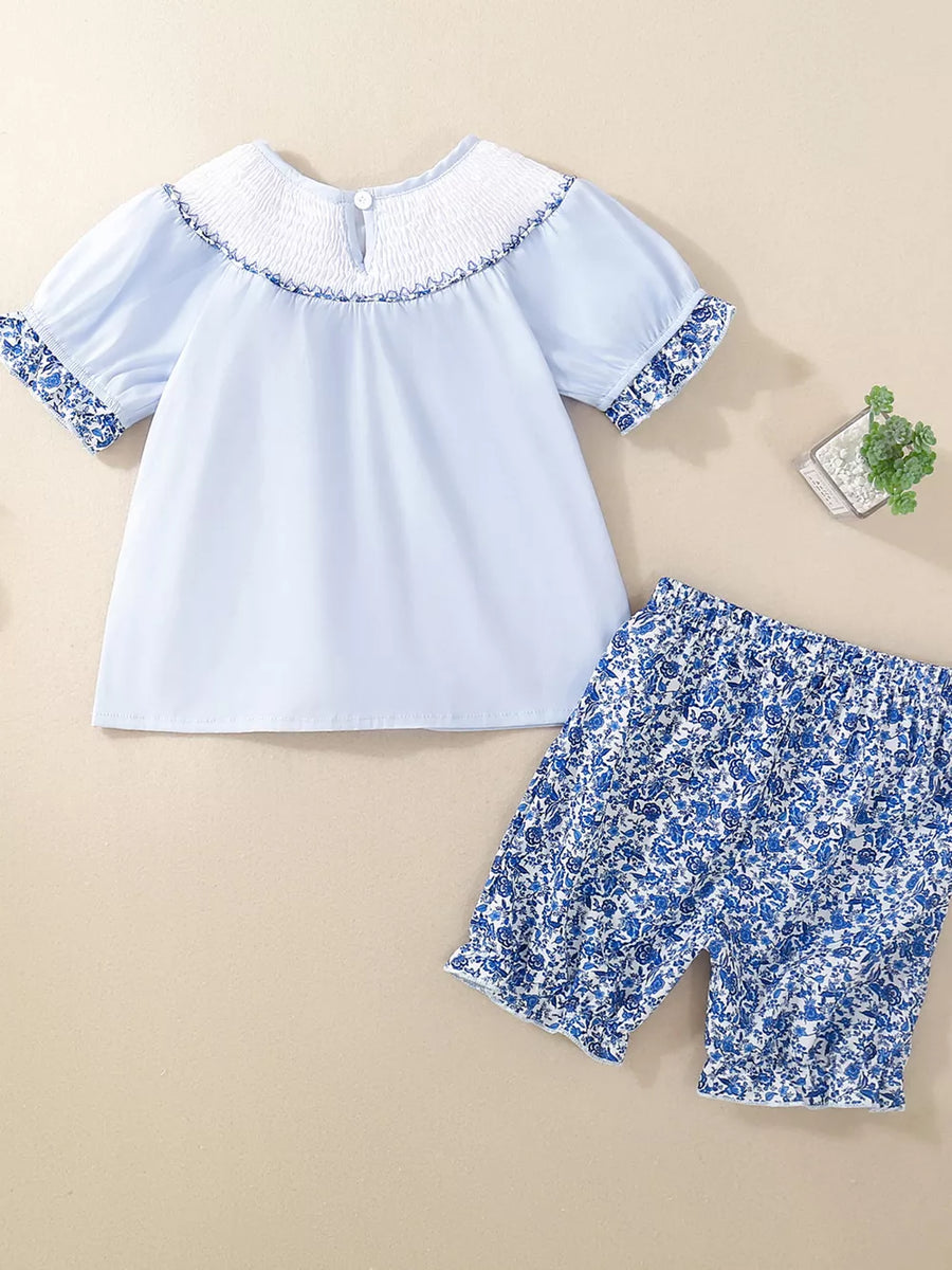 Baby blue cotton set with smocked white neckline and floral print shorts and sleeves.