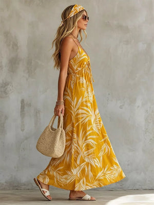 Yellow spaghetti strap maxi dress with tropical leaf print, tie front, and flowing skirt.