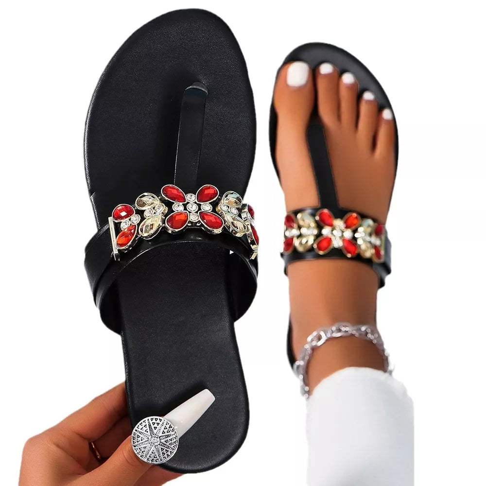 Black jeweled toe-post flat sandals with red and gold floral embellishments.