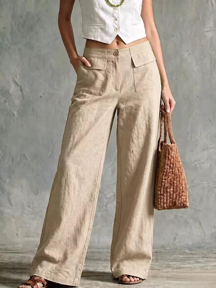 Linen wide-leg pants in beige with flap pockets and a button closure, styled with a white vest and woven bag.