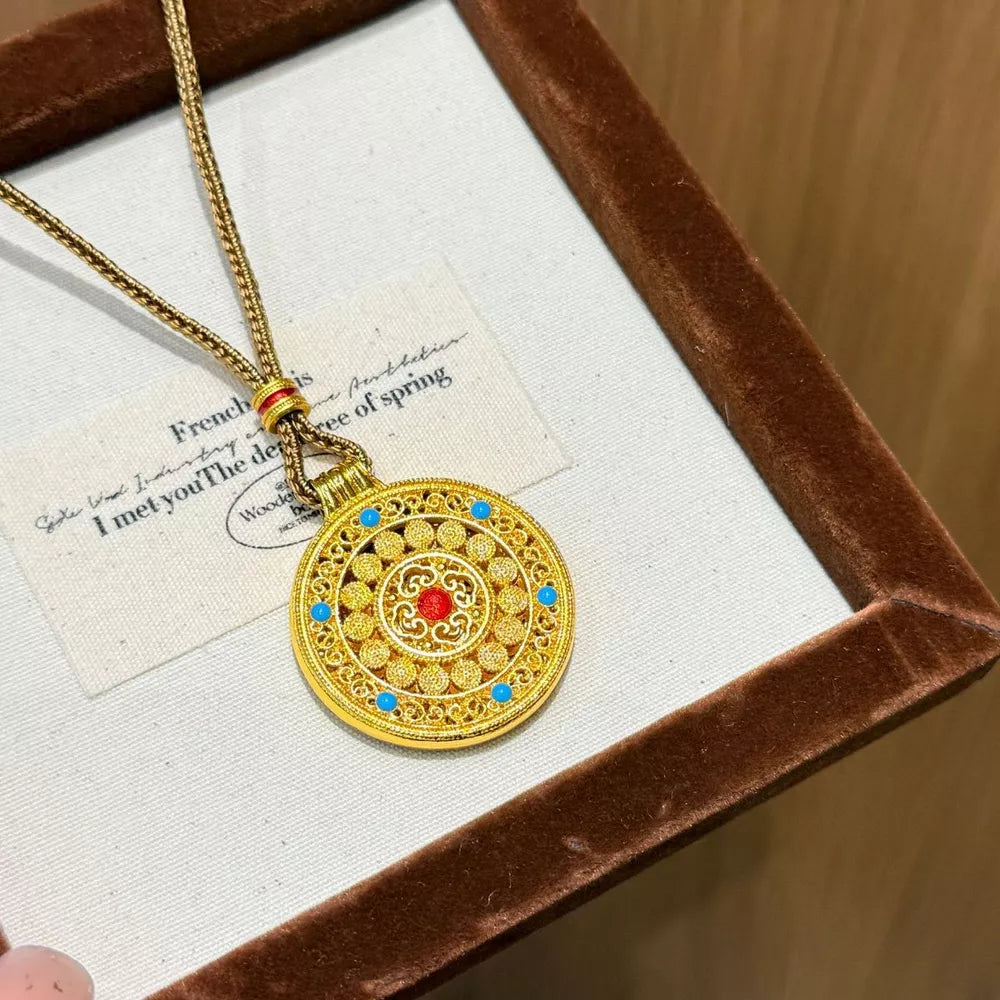 Gold-plated round pendant necklace with red and blue accents, artisanal design.