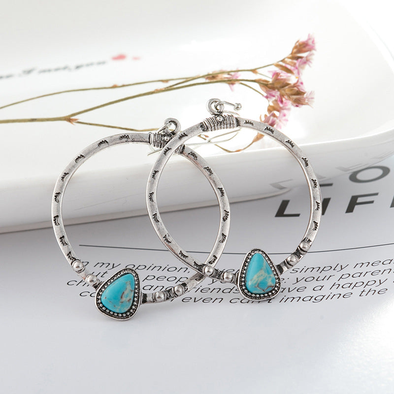 Southwestern stone hoop earrings in silver with turquoise teardrop accents and etched detailing.