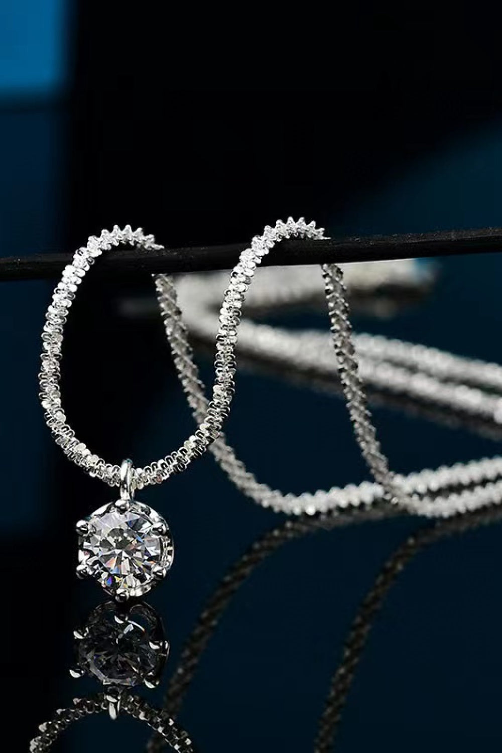 Silver pendant necklace with a textured chain and a round moissanite stone.