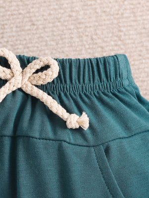 Teal cotton shorts with elastic waistband and cream rope drawstring detail.
