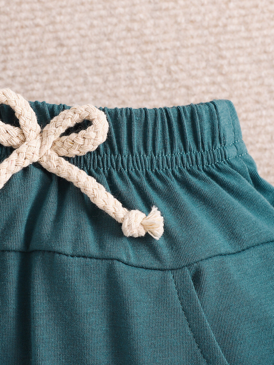 Teal cotton shorts with elastic waistband and cream rope drawstring detail.