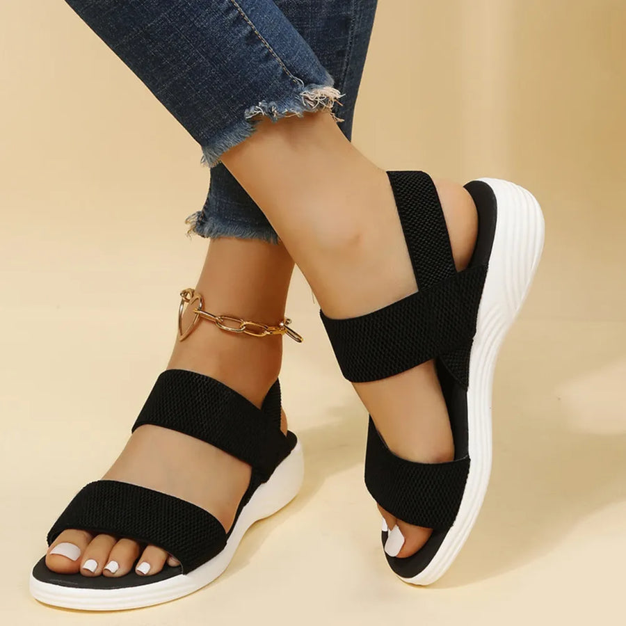 Black knit strap sandals with white soles and a gold heart anklet.