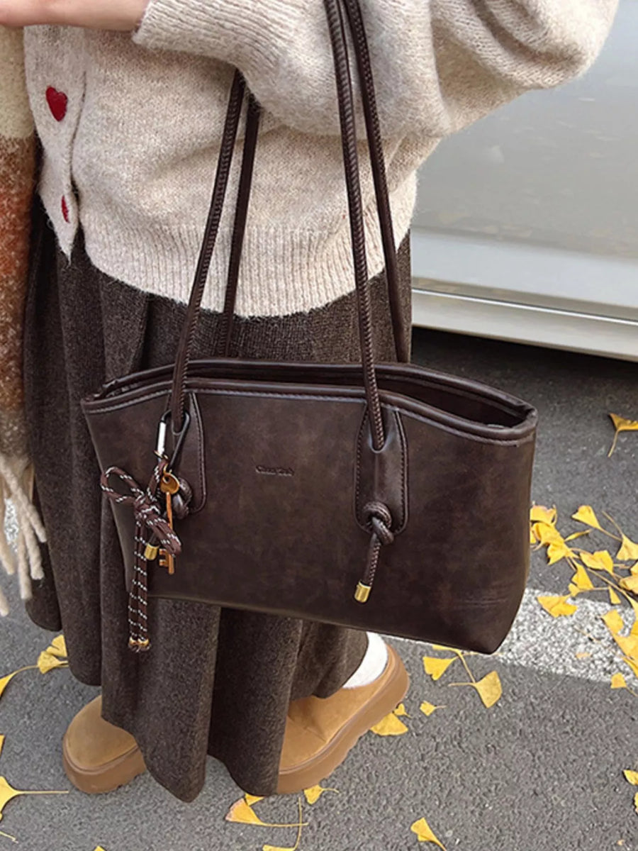 Brown leather shoulder bag with braided straps and decorative keys.