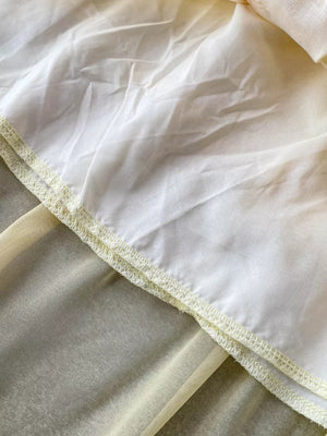 Floral ruffled two-piece ensemble detail showing sheer yellow fabric layered under white with decorative stitching.