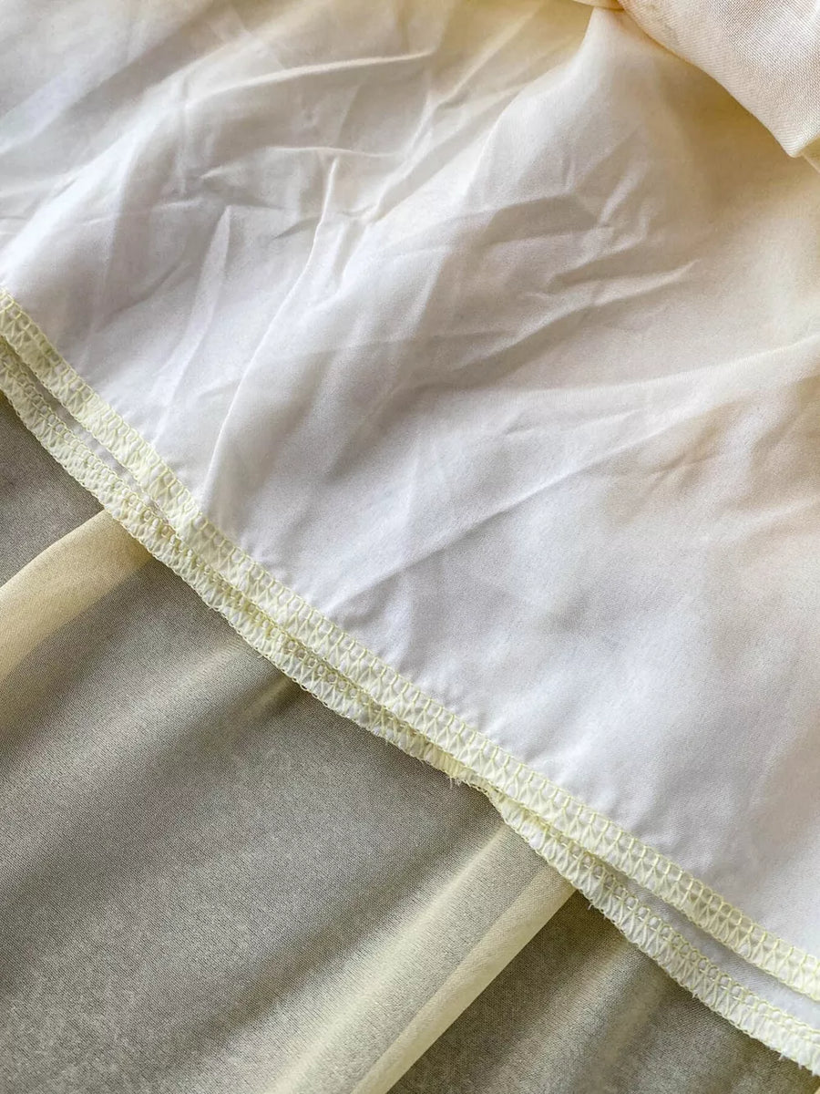 Floral ruffled two-piece ensemble detail showing sheer yellow fabric layered under white with decorative stitching.
