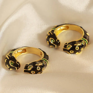 Gold panther head open ring with black enamel and green gemstone accents.