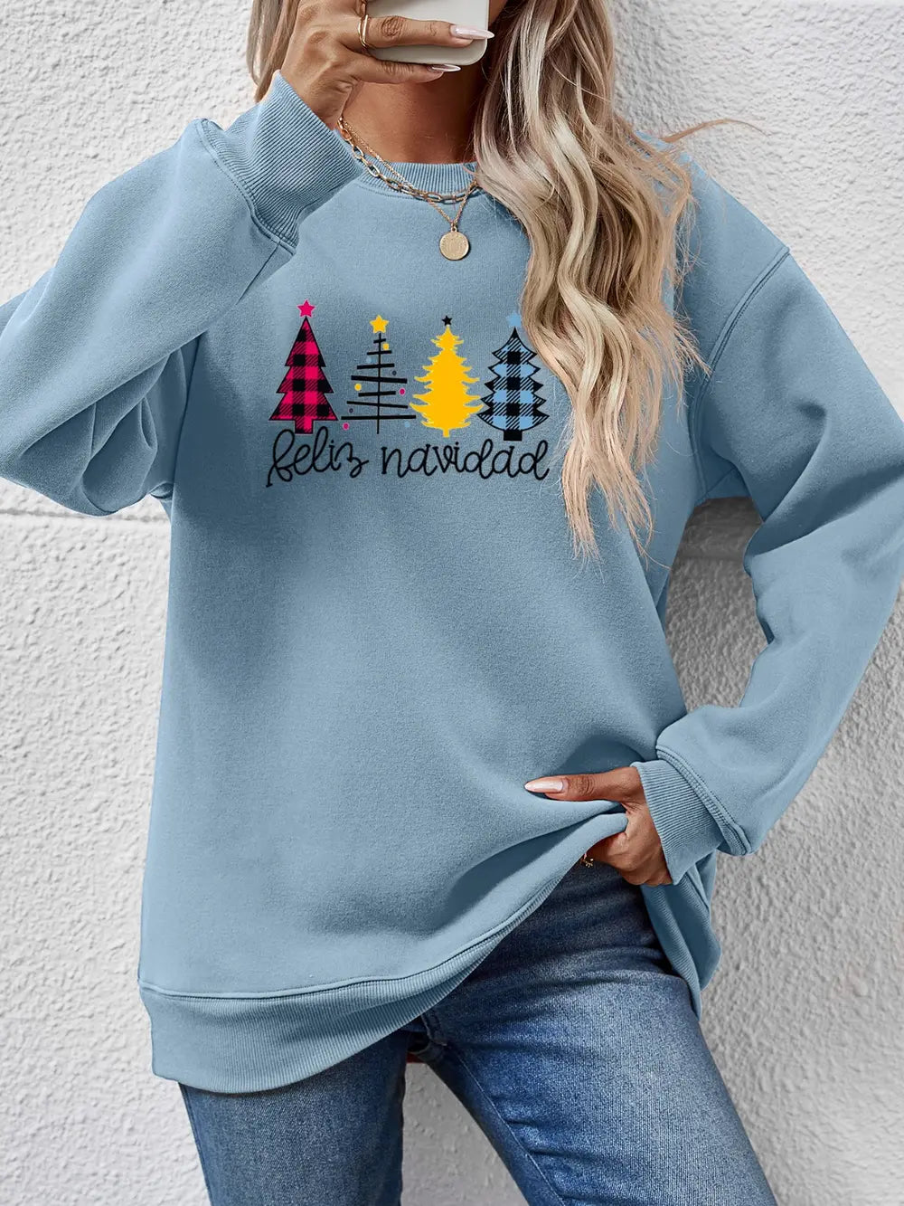 Feliz Navidad graphic crewneck sweatshirt in Misty Blue with festive Christmas trees and plaid patterns.