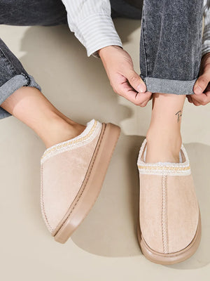 Tan shearling house slippers with embroidered trim and plush lining.