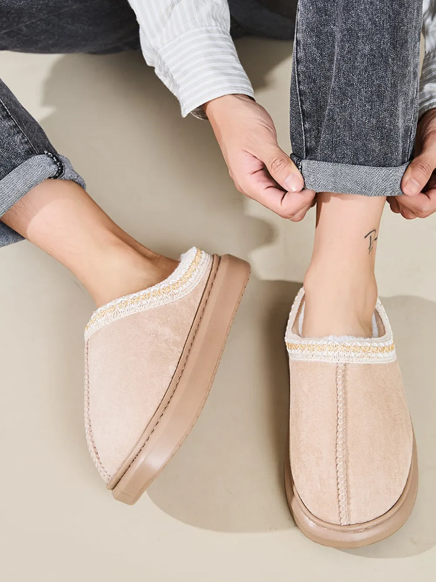 Tan shearling house slippers with embroidered trim and plush lining.