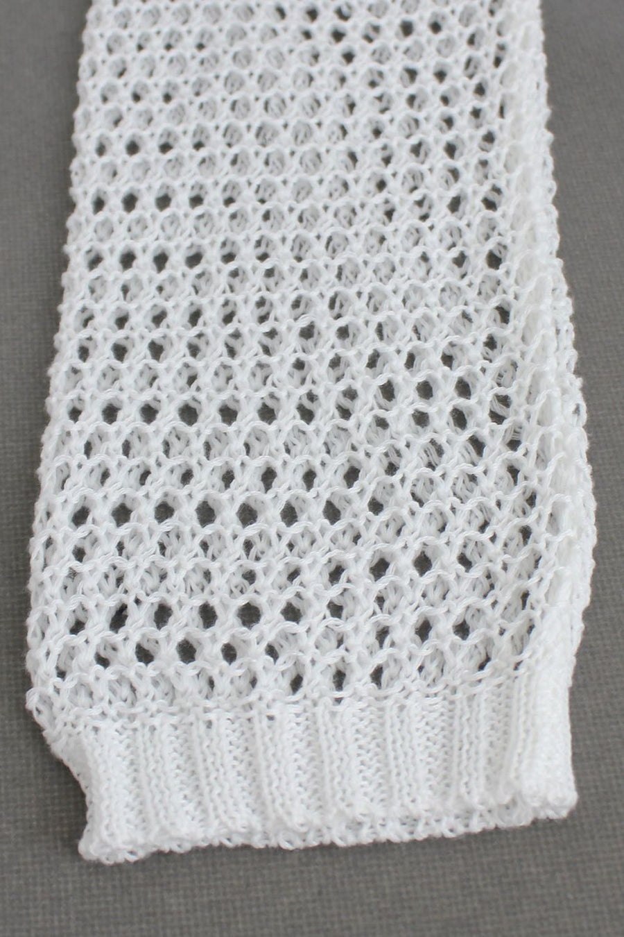 White crochet blouse with open knit pattern and ribbed hem detail.