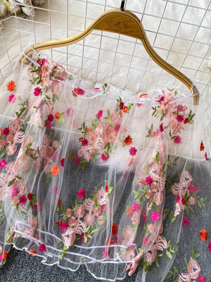 White off-shoulder t-shirt with colorful floral embroidery and ruffled hem.