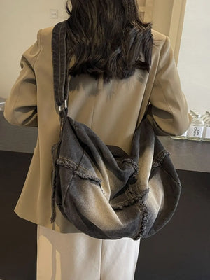 Frayed denim slouch crossbody bag in dark wash with distressed edges.