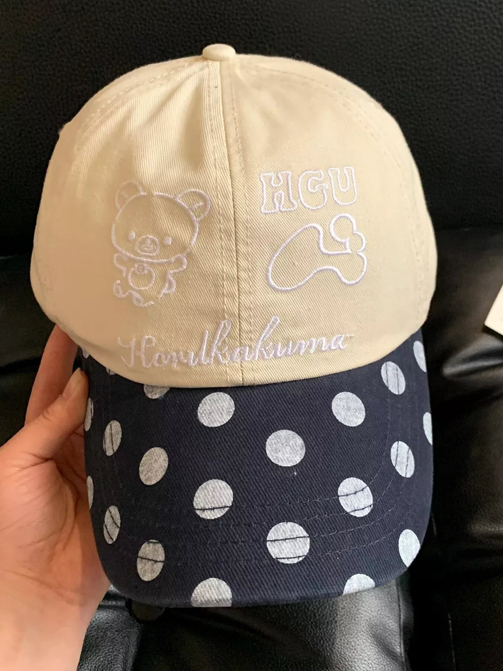 Cap with beige crown featuring embroidered bear and text, and navy brim with white polka dots.