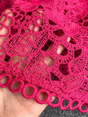 Fuchsia pink lace dress detail with cutout pattern and circular trim.