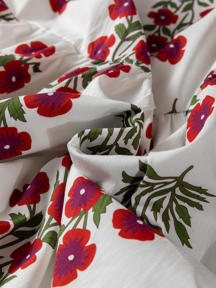 V-neck mini dress in white cotton with a red and purple floral print and green leaves.