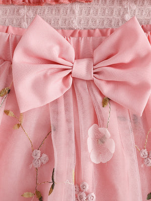 Pink smocked off-shoulder top and tulle skirt set with floral embroidery and bow detail.
