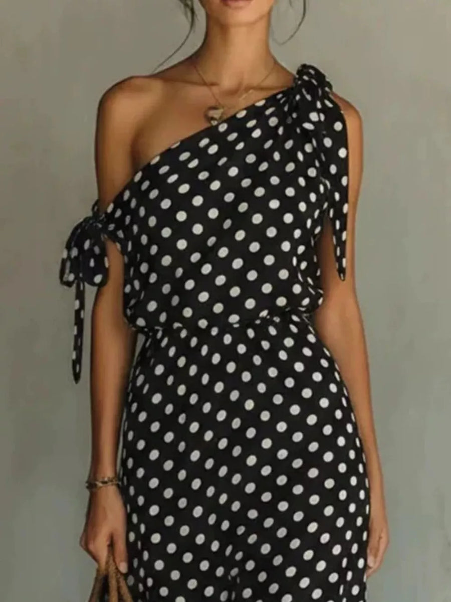 Black polka dot one-shoulder maxi dress with cinched waist and tie details.