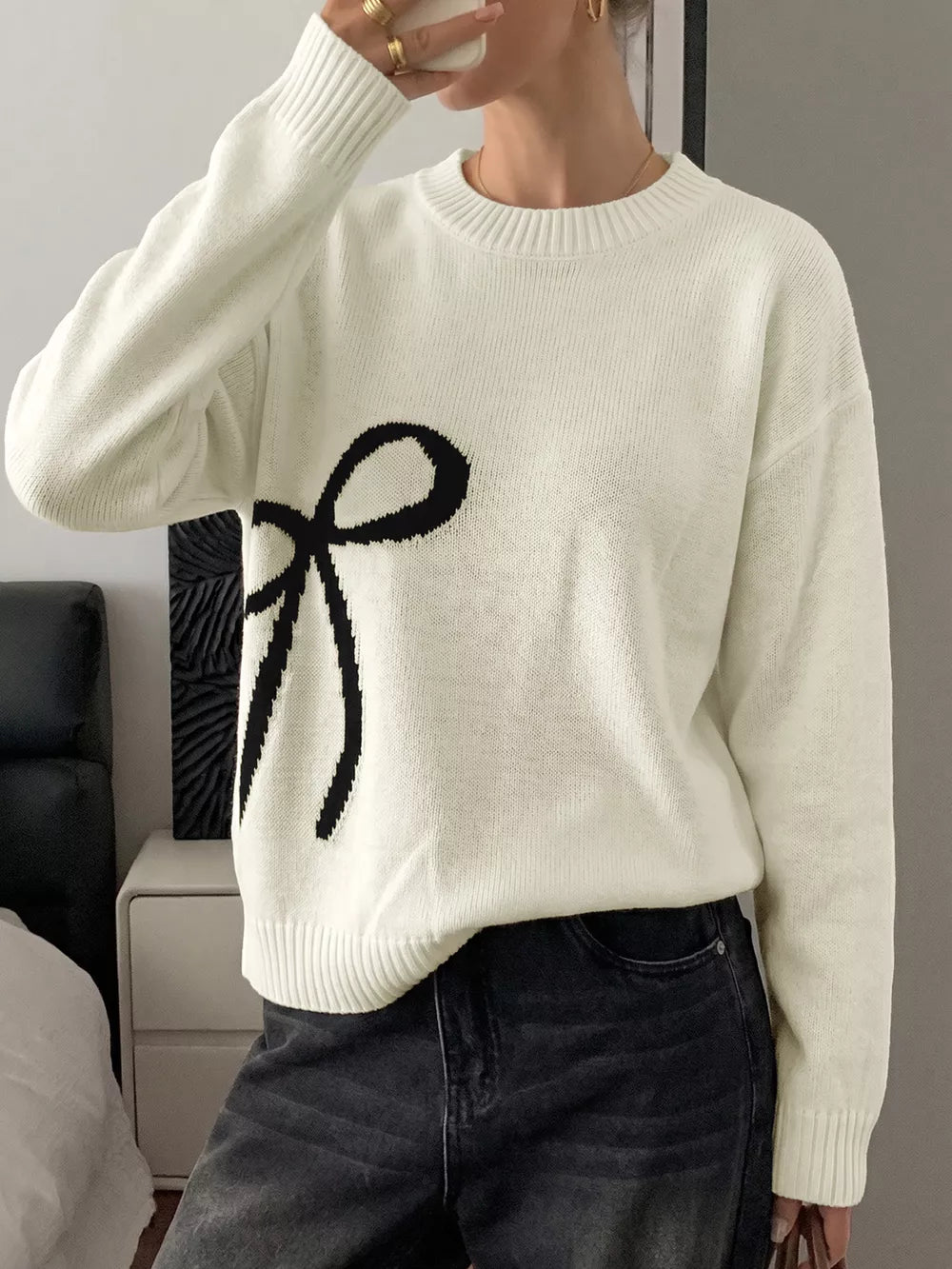 Cream knit sweater with black bow graphic, crew neck, long sleeves.