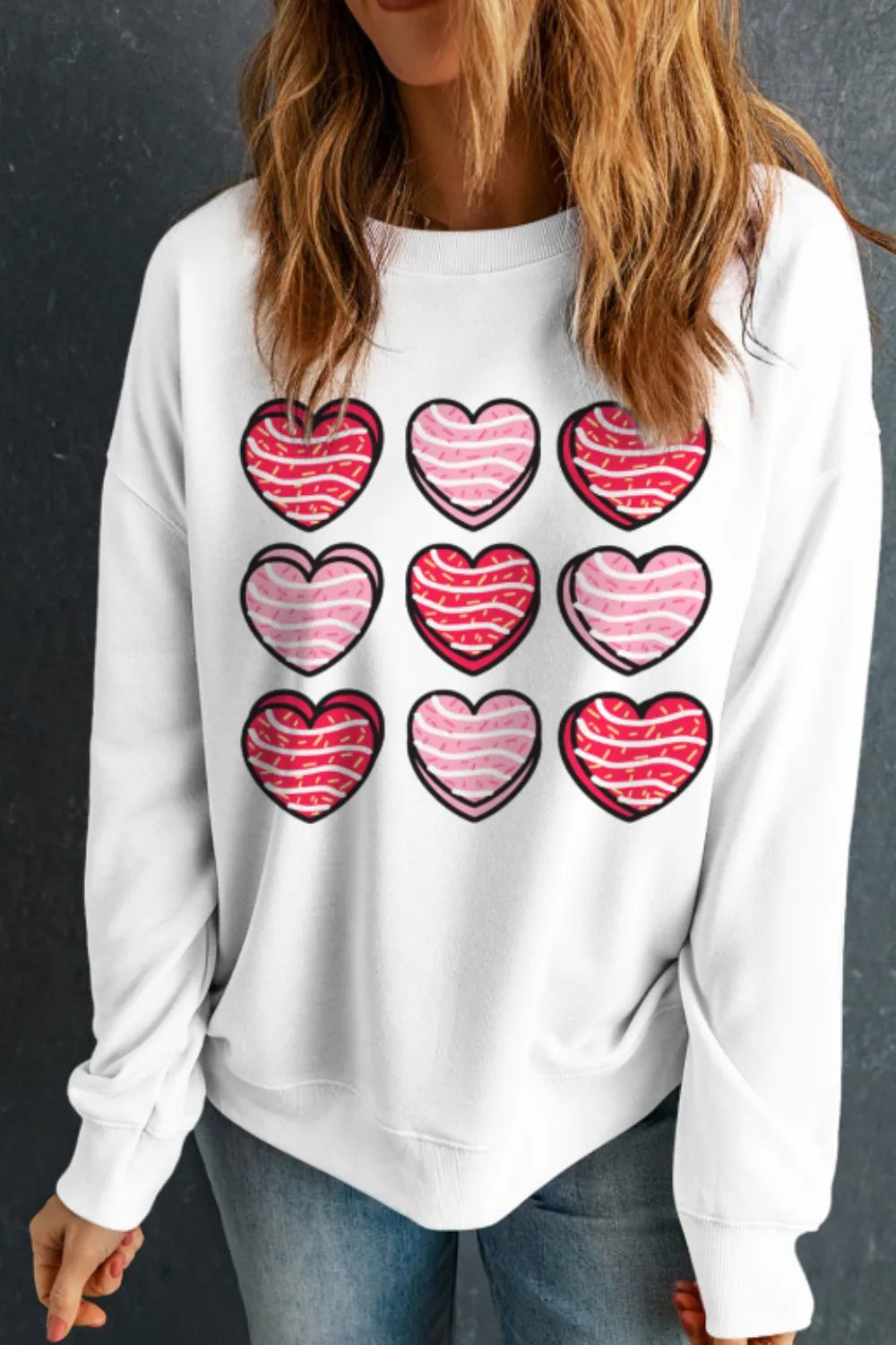 White crewneck sweatshirt with a grid of nine hearts graphic, featuring pink and red stripes.