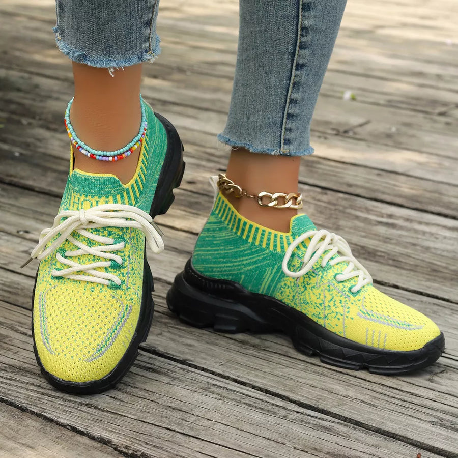 Vibrant two-tone yellow and green knit lace-up sneakers with chunky black soles and ankle chains.