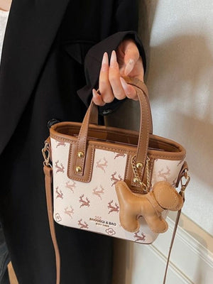 Charming mini crossbody bag with deer print and dog charm, in blush pink.