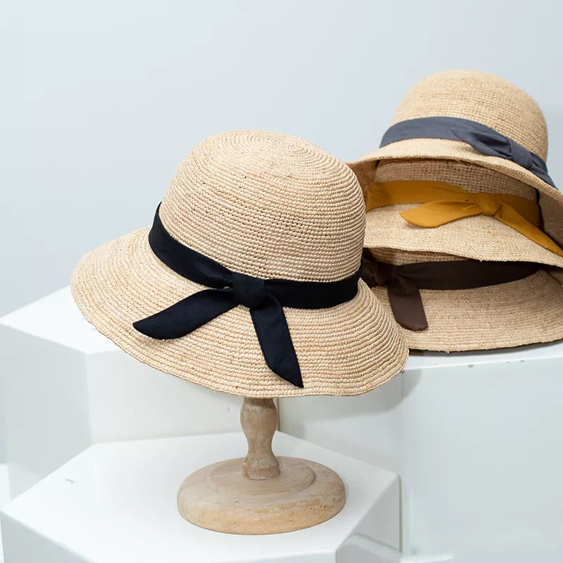 Chic wheat straw sun hat with black bow detail, on display with other colored bow hats.