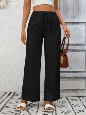 Black high-waist wide-leg pants with drawstring and pockets, styled with slides.