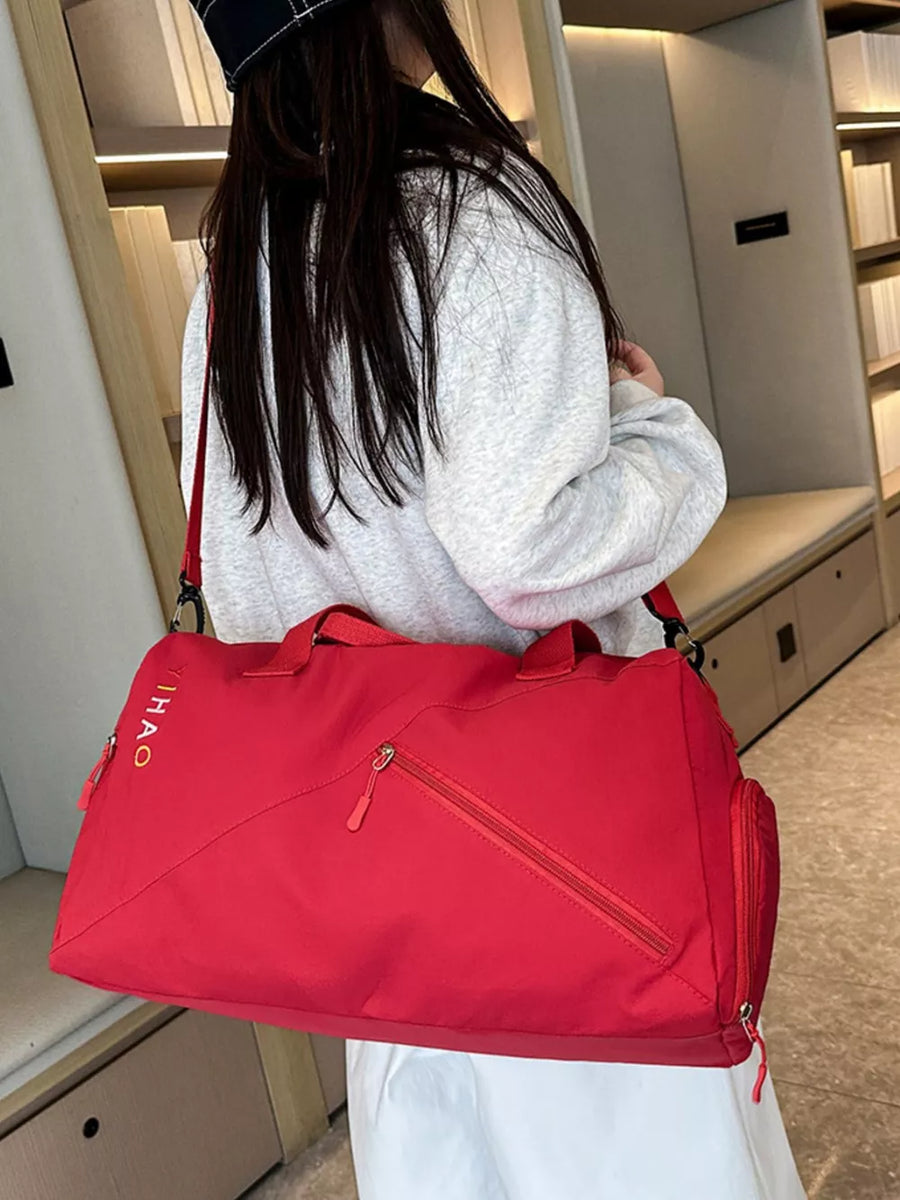 Red duffel bag with diagonal zip pocket and side pouch, embroidered logo detail.