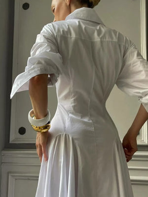 White cotton shirt dress with gathered skirt and rolled sleeves, styled with bold bracelets.