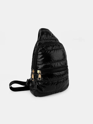 Glossy padded sling bag in black with gold zippers and adjustable strap.