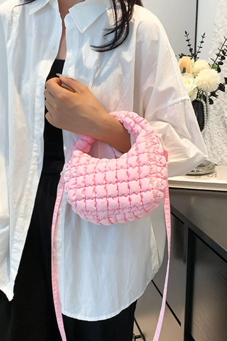 Pink padded crescent crossbody bag with sculptural texture and a long strap.