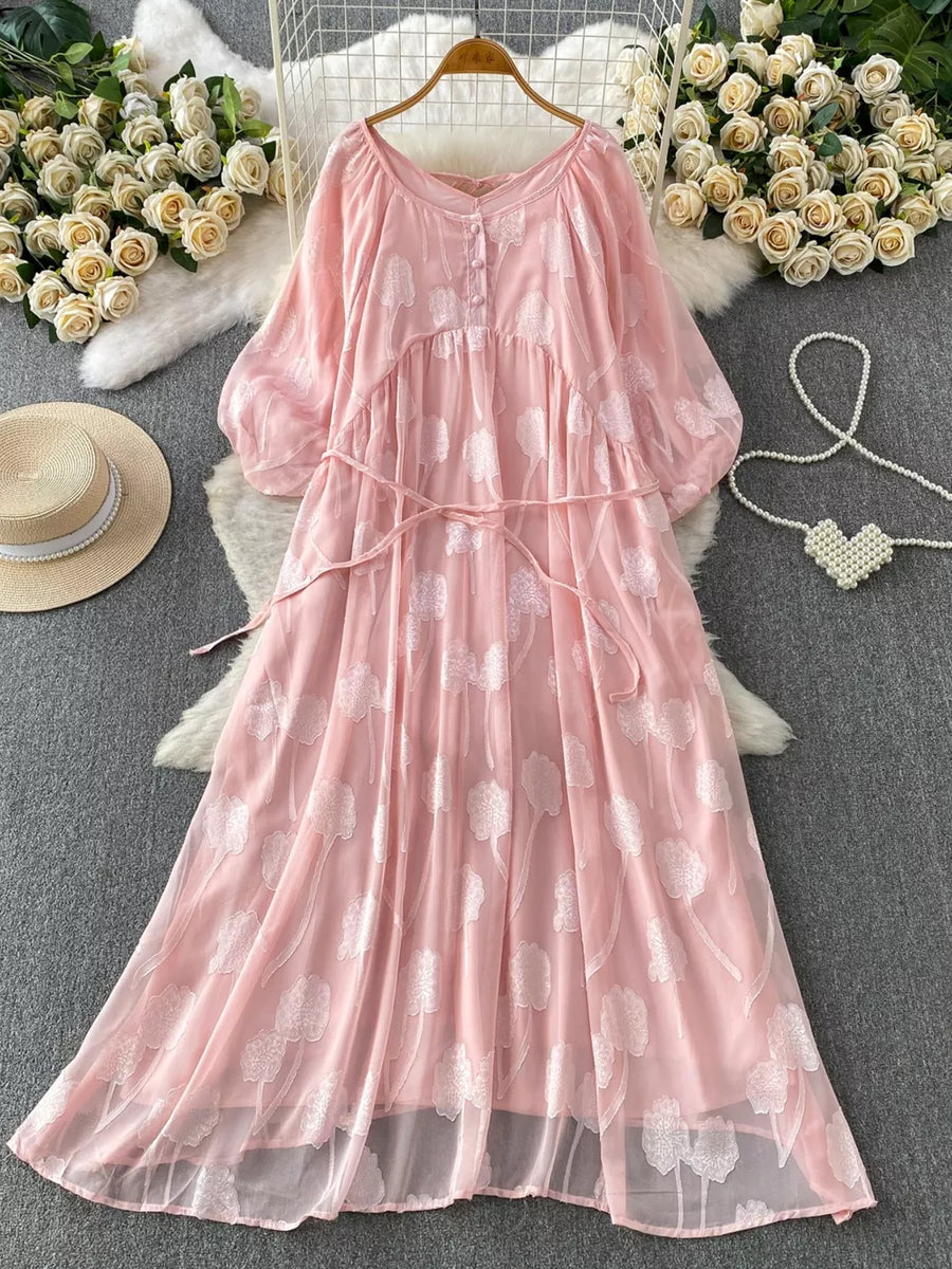 Pink chiffon maxi dress with floral embroidery, V-neck, button-down front, and belted waist.