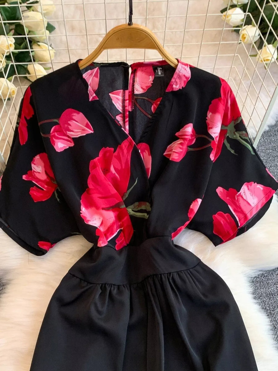 Black wide-leg romper with abstract red floral print, V-neck, short sleeves, and pockets.