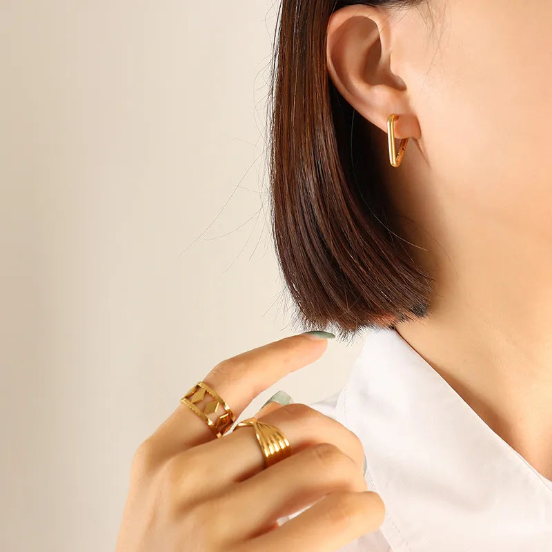 Gold Wide Triangle huggie earrings made of steel, worn with matching geometric rings.