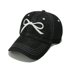 Black denim baseball cap with white embroidered bow detail and contrast stitching.
